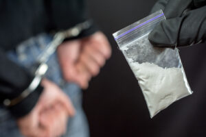 Police arrest drug trafficker with handcuffs. police officer finds A Little Bag Of Drugs during a search
